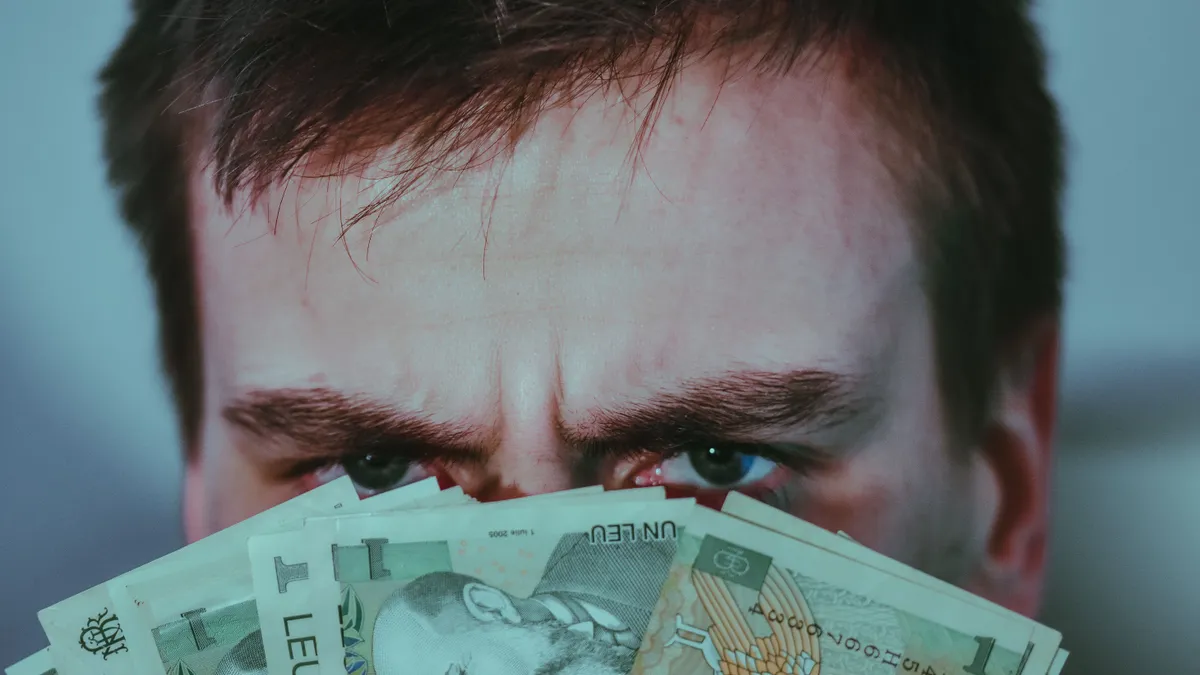 Un bărbat privește îngrijorat peste un evantai de bancnote de un leu.