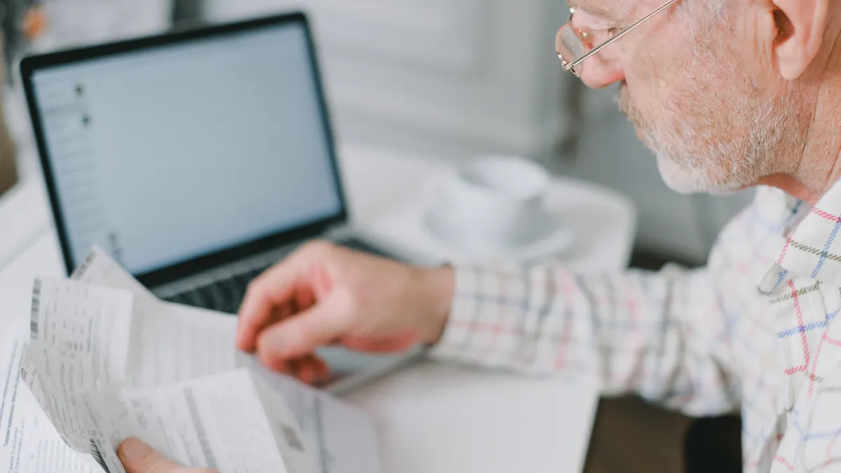 Pensionar care verifică acte, în fața unui laptop