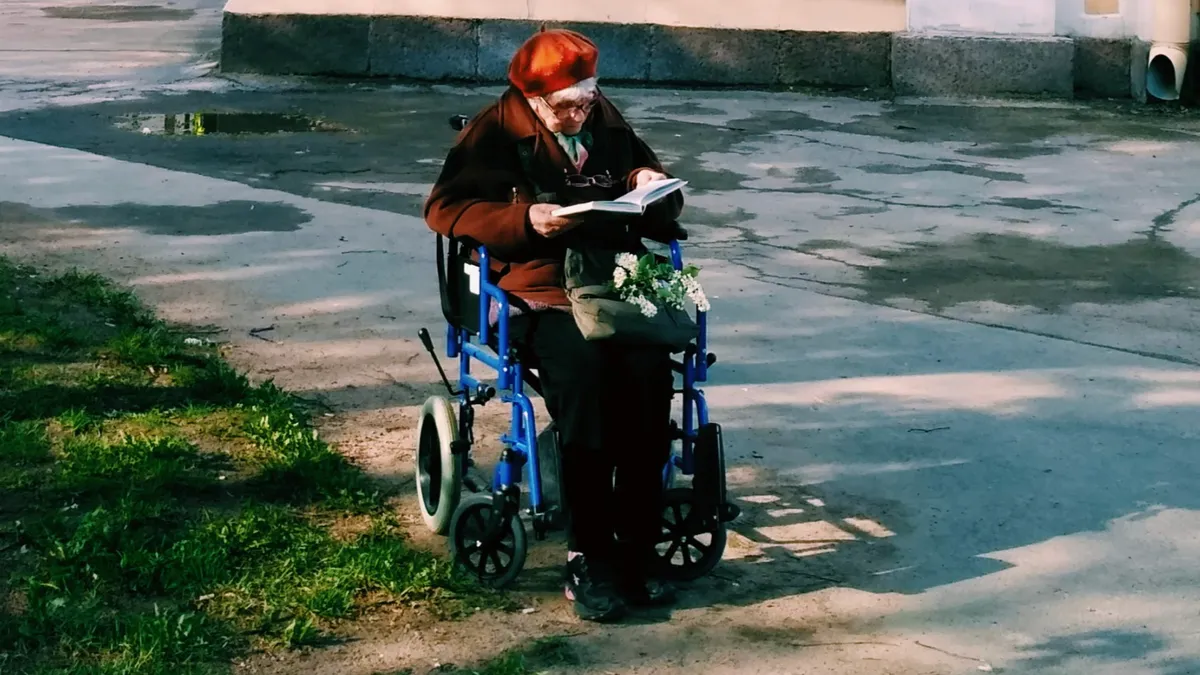 O bătrână într-un scaun cu rotile citește o carte