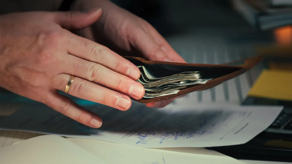 Portofel cu bancnote, ținut deasupra unor documente.