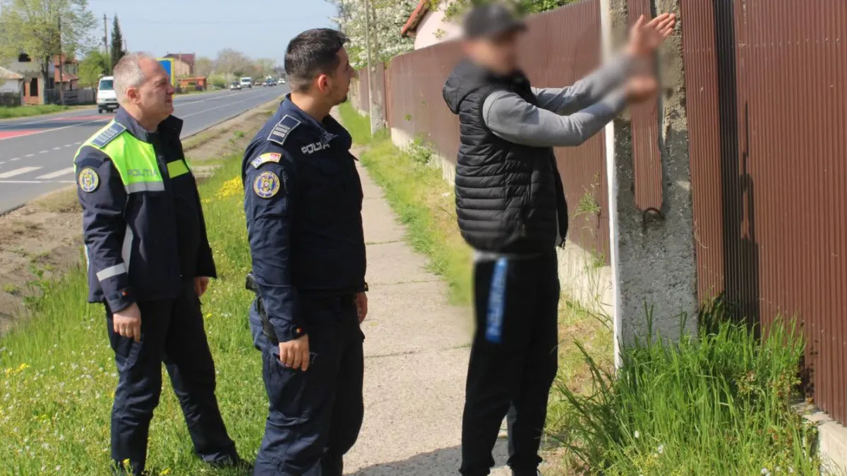 doi polițiști escortează un bărbat care ridică mâinile pentru a indica un gard