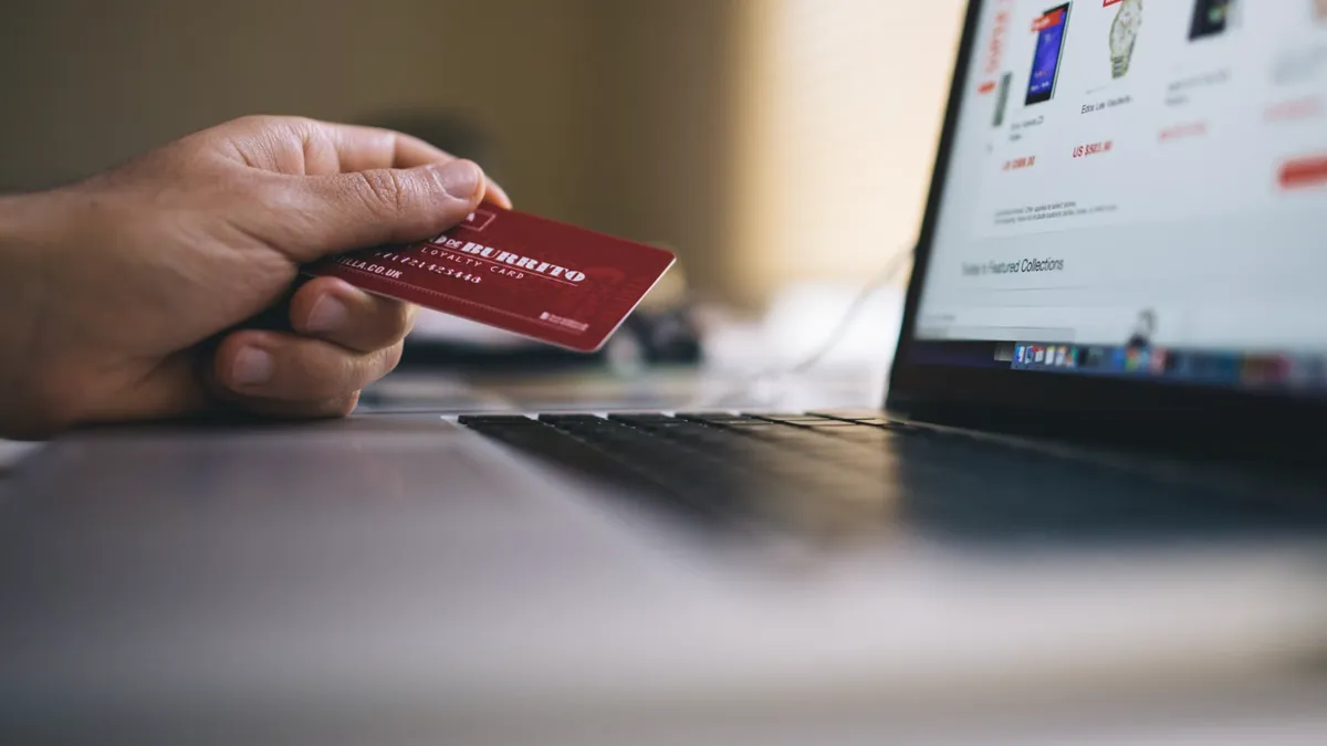O persoană ține un card bancar deasupra tastaturii în timp ce face cumpărături online