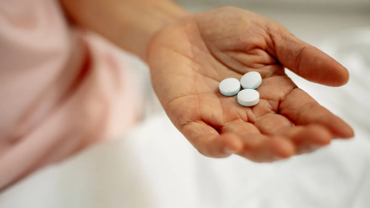 Persoană vârstnică ținând medicamente în palmă