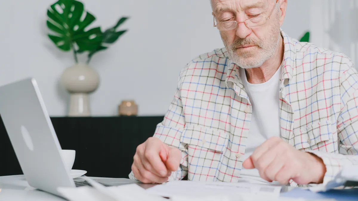 Pensionar care verifică documente într-un birou.