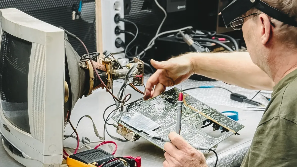 Un tehnician lucrează la componente electronice într-un atelier, concentrat pe repararea plăcilor de circuit